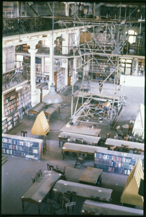 Library interior with rows of tables, bookshelves, and scaffolding.