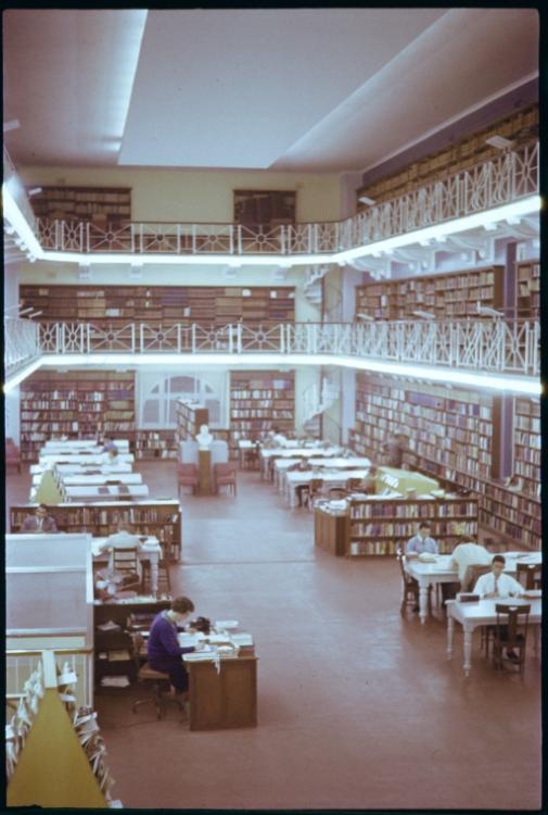 Interior of a two-story library with bookshelves, tables, and people reading.