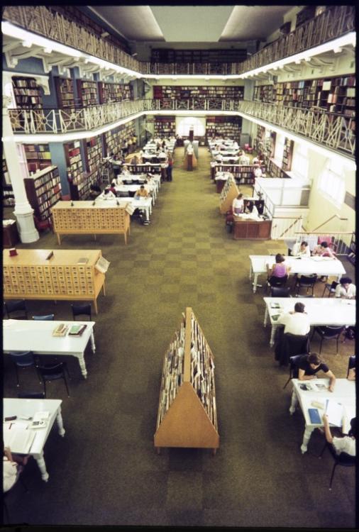 A large, multi-level library interior with many tables and bookshelves.