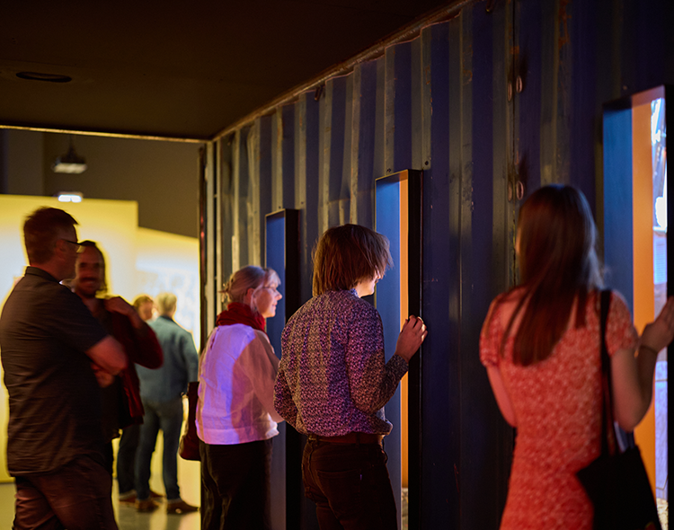 People looking into an image slideshow through windows cut into the side of a sea container