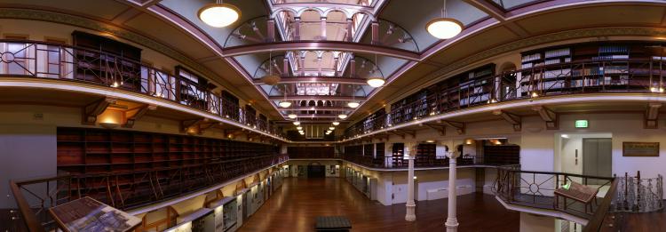 Interior of an ornate, two-level library hall with bookshelves, decorative railings, and hanging lights.