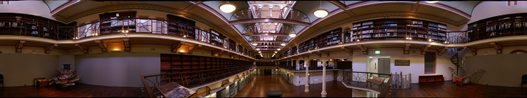 Interior of an ornate, two-level library hall with bookshelves, decorative railings, and hanging lights.