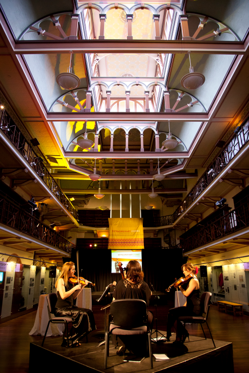 3 musicians seated in an ornate multi-level gallery space