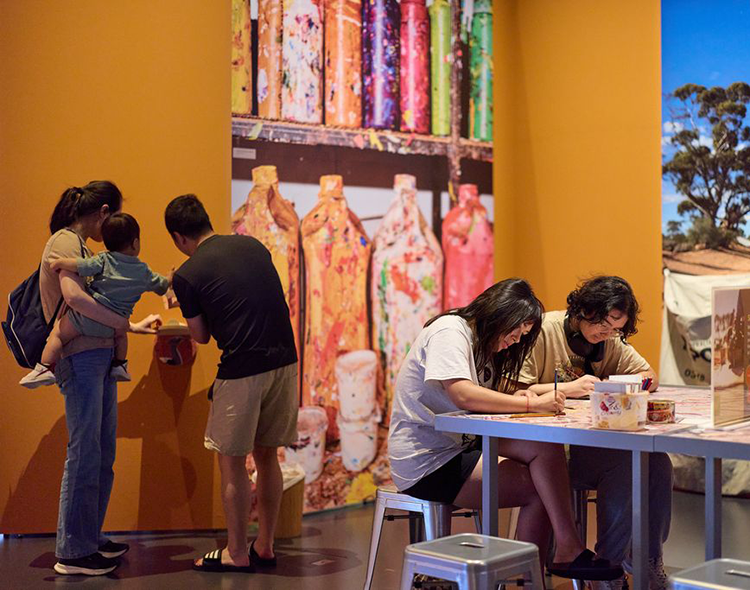 People engaged in creative activities in a Museum gallery with a mural of colourful bottles.