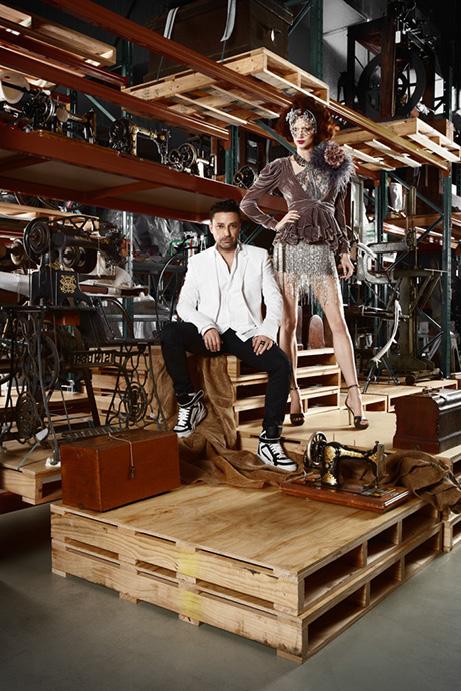 Two people in a vintage warehouse, surrounded by sewing machines, wearing fashionable outfits.