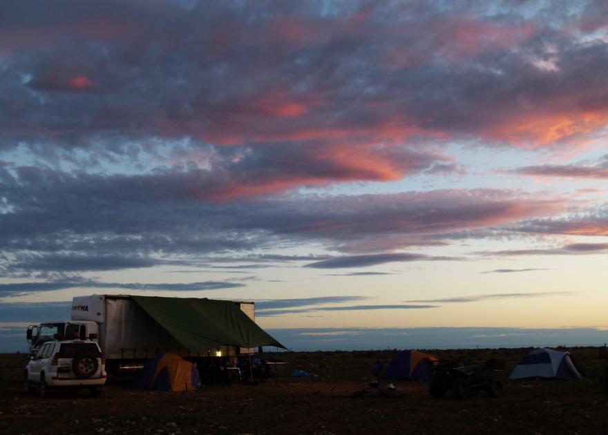 A campsite set up beneath a beautiful sunset on an expansive plain
