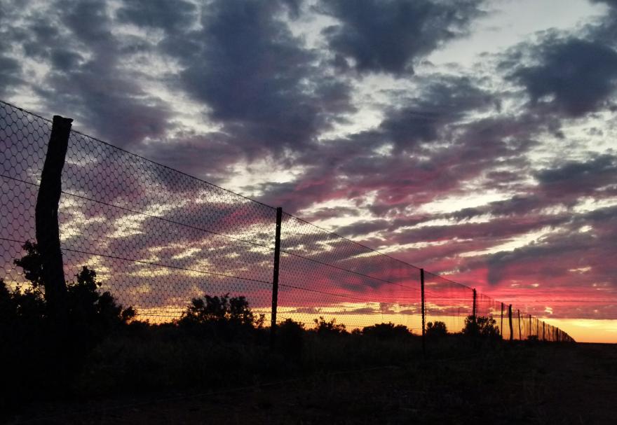 A fence beneath a dramatic cloudy sunset