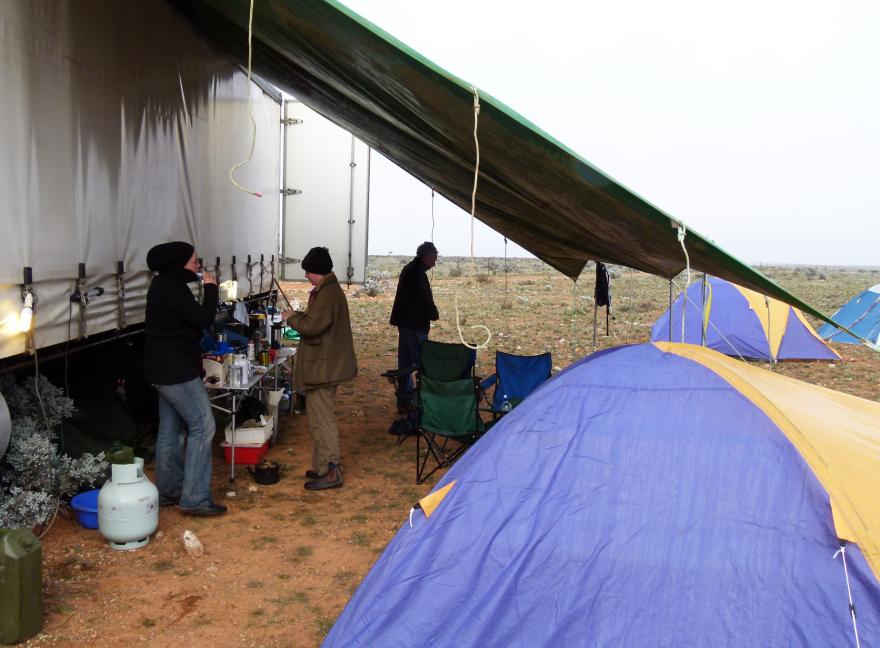 3 people getting ready for the day at a campsite with tents and other camping gear