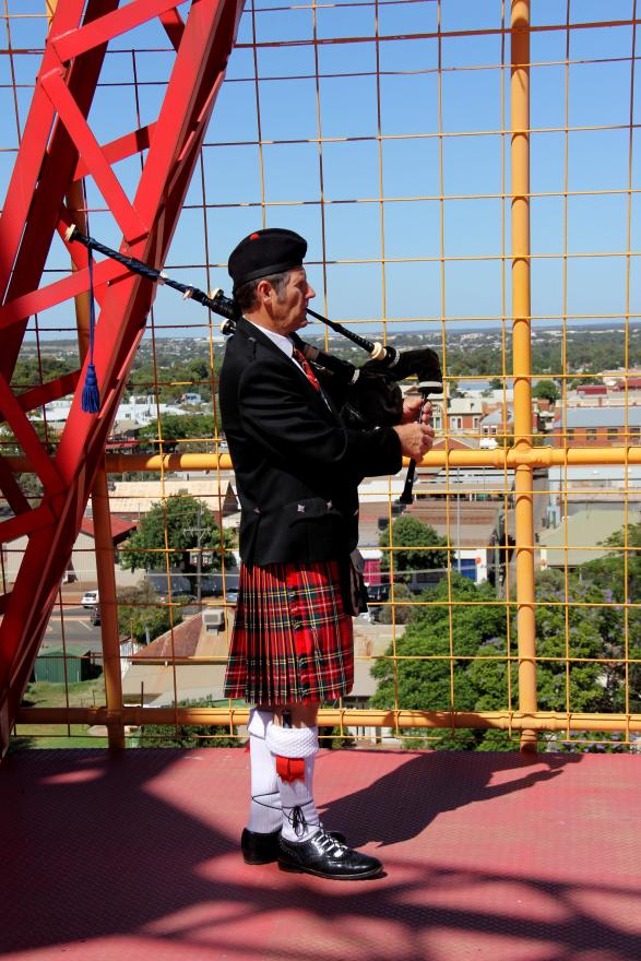 A person wearing traditional garb plays the bagpipes atop a headframe