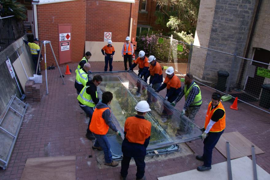 A group of people wearing high-viz lifting the lid of Megamouth's old tank