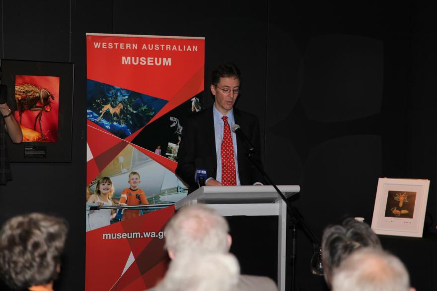 A person speaks at a podium with a Western Australian Museum banner behind him.
