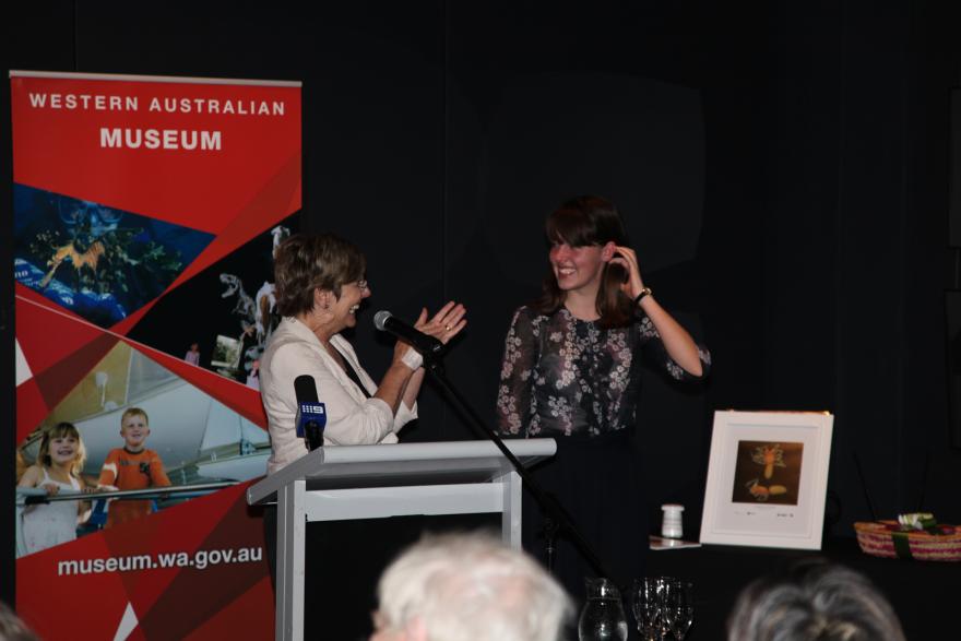 Two people talking at a lectern with a Western Australian Museum banner in the background.