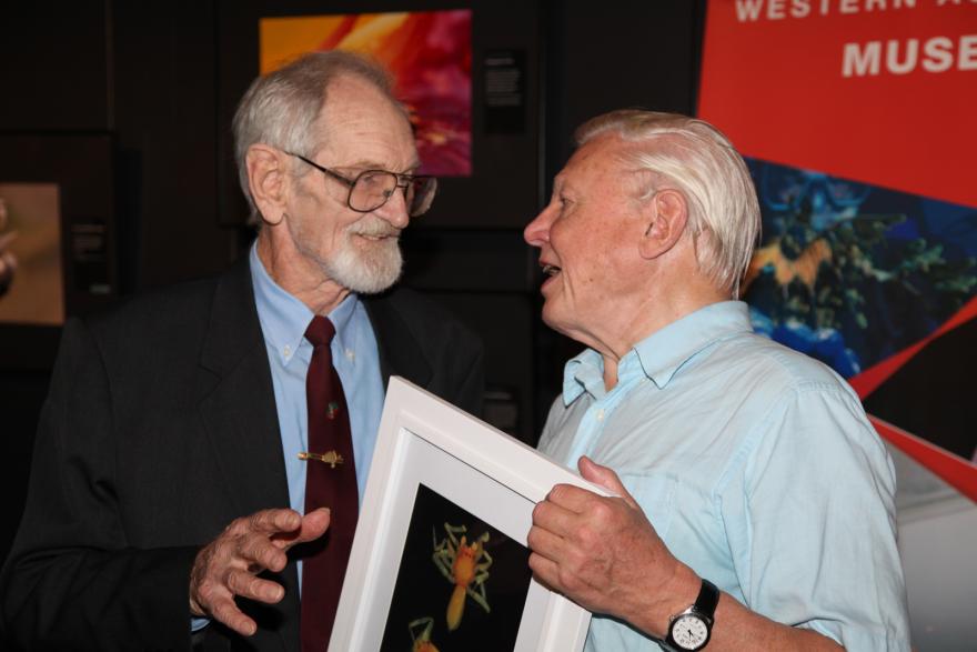 Two people in conversation, one holding a framed picture.