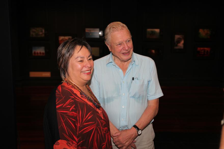 Two people smiling in a gallery with framed photos on the wall behind them.