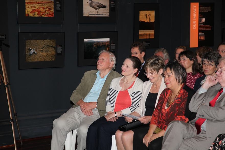 Group of people seated in a room with wildlife photographs displayed on the walls.