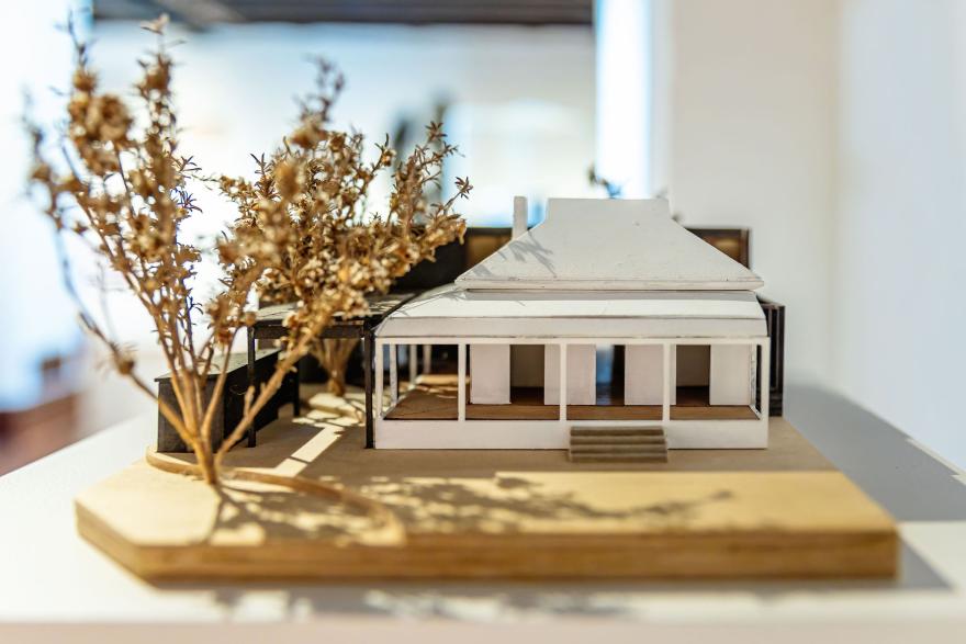 A small diorama of a white house with a wrap-around veranda and a brown tree