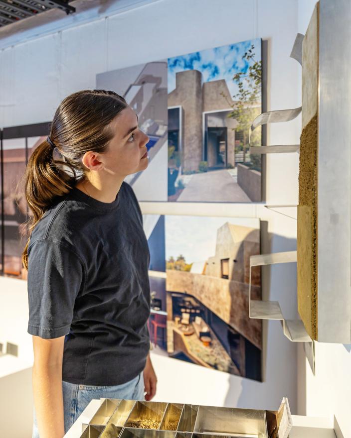 A person with brown hair and a black t-shirt looks at a 3-d sculpture hanging from a wall in a gallery