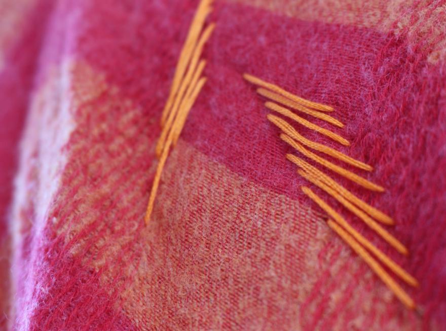 Close-up of red fabric with orange stitches.