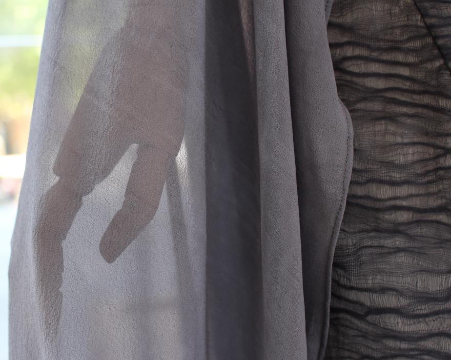 Shadow of a hand seen through translucent gray fabric, with wrinkled fabric on the right side.