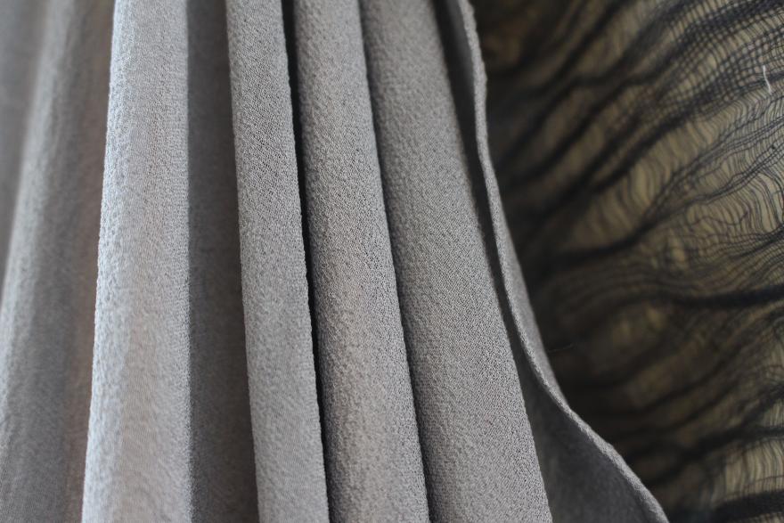 Close-up of folded grey fabric next to sheer black fabric with wavy lines.