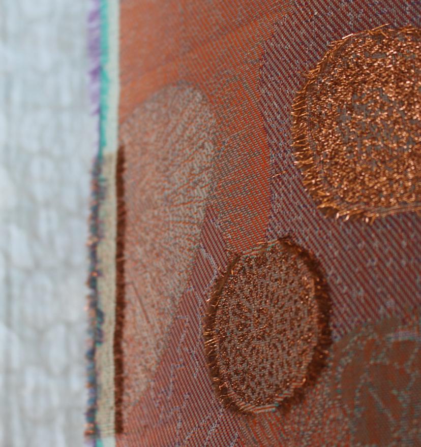 Close-up of a textile with rust-coloured circles and metallic embroidery.