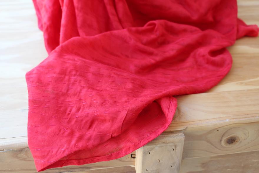 Red fabric with stitching on a light wooden surface.