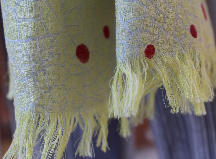 Close-up of a light green fringed fabric with red circular patterns.