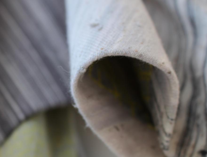 Close-up view of folded, textured grey fabric with striped fabric in the background.