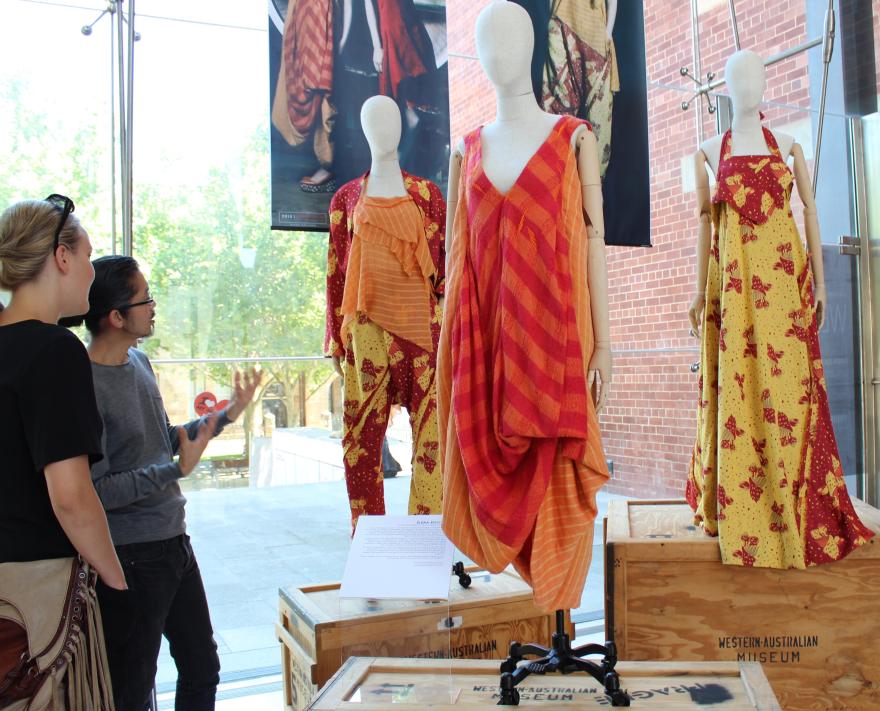 A museum exhibit featuring three mannequins in colourful traditional garments, with two people observing.