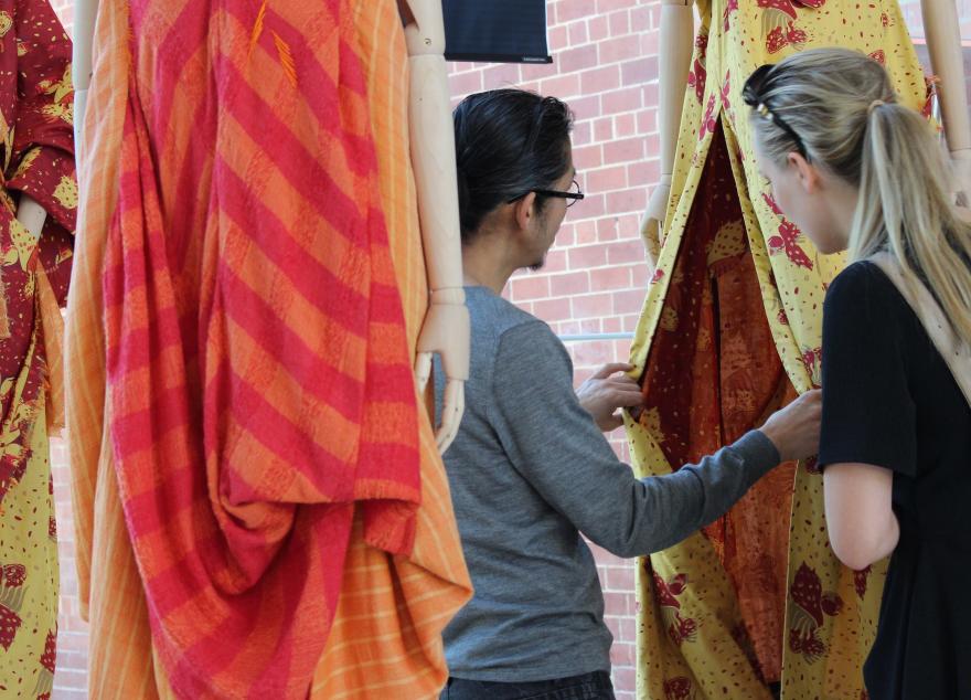 Two people examine vibrant fabric on a mannequin in an indoor setting.