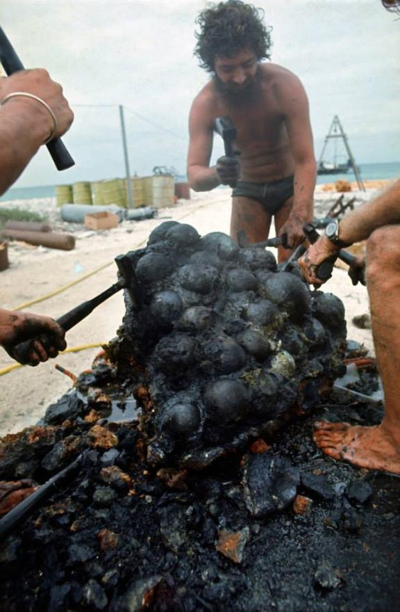 People examining a large, cannonball-like cluster near a beach.