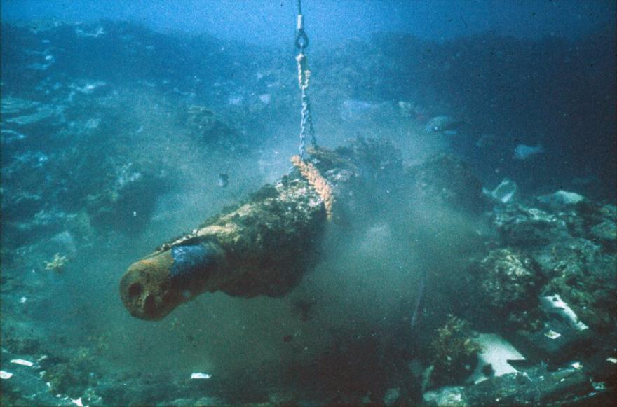 Underwater image of an old cannon being lifted by a chain.