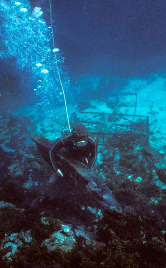 Scuba diver underwater with debris and a metal structure in the background.