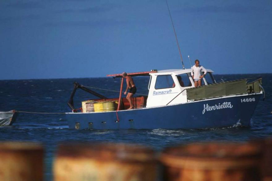 A blue and white fishing boat named "Henrietta" on the ocean with two people aboard.