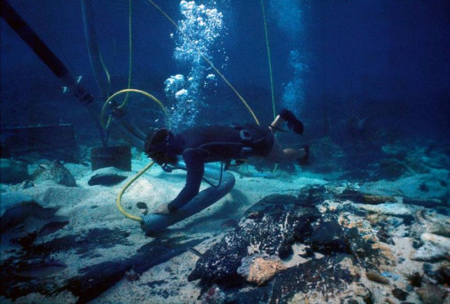 Diver in scuba gear exploring the ocean floor with hoses releasing bubbles.