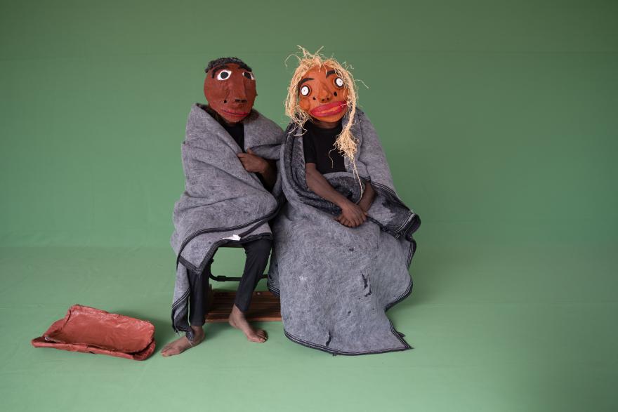 Two Aboriginal people with Paper Mache cartoon heads sitting in front of a green screen