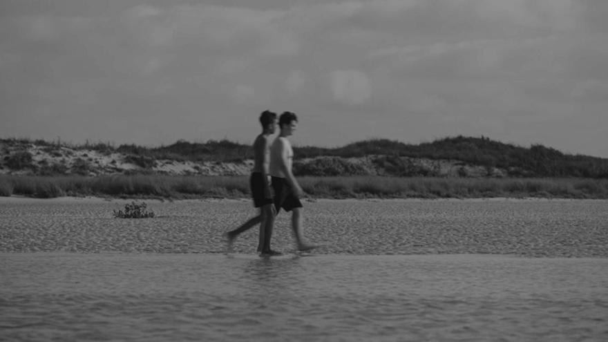 Black and white still of two boys walking across a beach