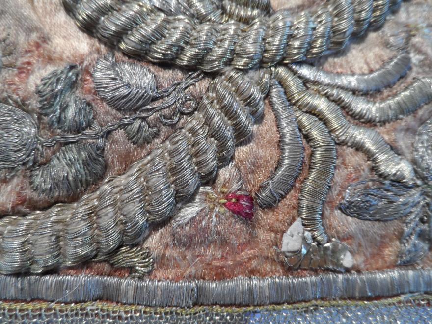 Close-up of silver metallic embroidery on a textured fabric background.