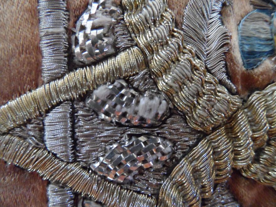Close-up of intricate silver and gold metallic embroidery on fabric.