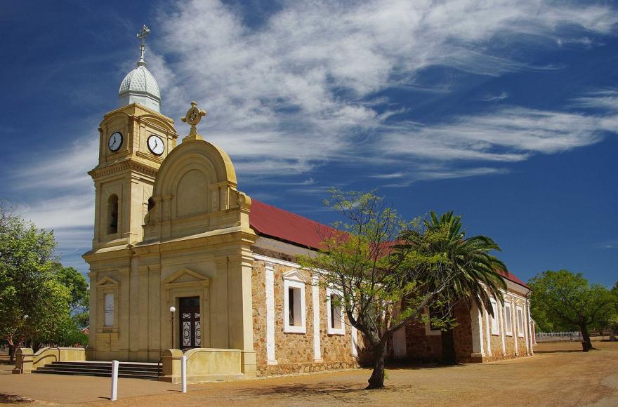 Historic church with clock tower, stone walls, and red roof under a blue sky.