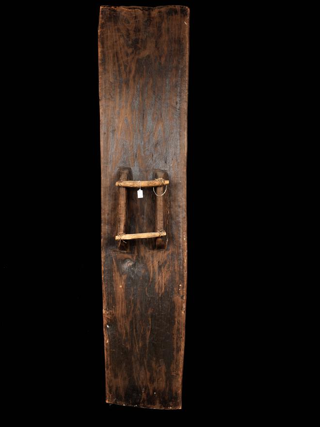 A large, colourful war shield from Kupkein, Upper Sepik. Features a smiling face with six black circles below. Back view.