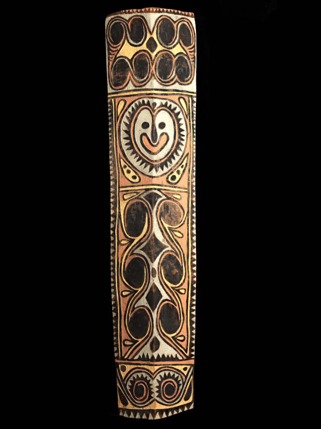 A large, colourful war shield from Kupkein, Upper Sepik. Features a smiling face with six black circles below. Front view.