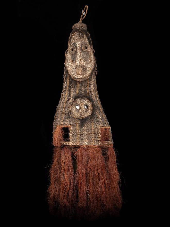 A double faced, tall woven dance mask from Kanganaman Village. The mask has two hand holes, a raffia skirt, and two holes in the lower face for the dancer to see out. Front View.