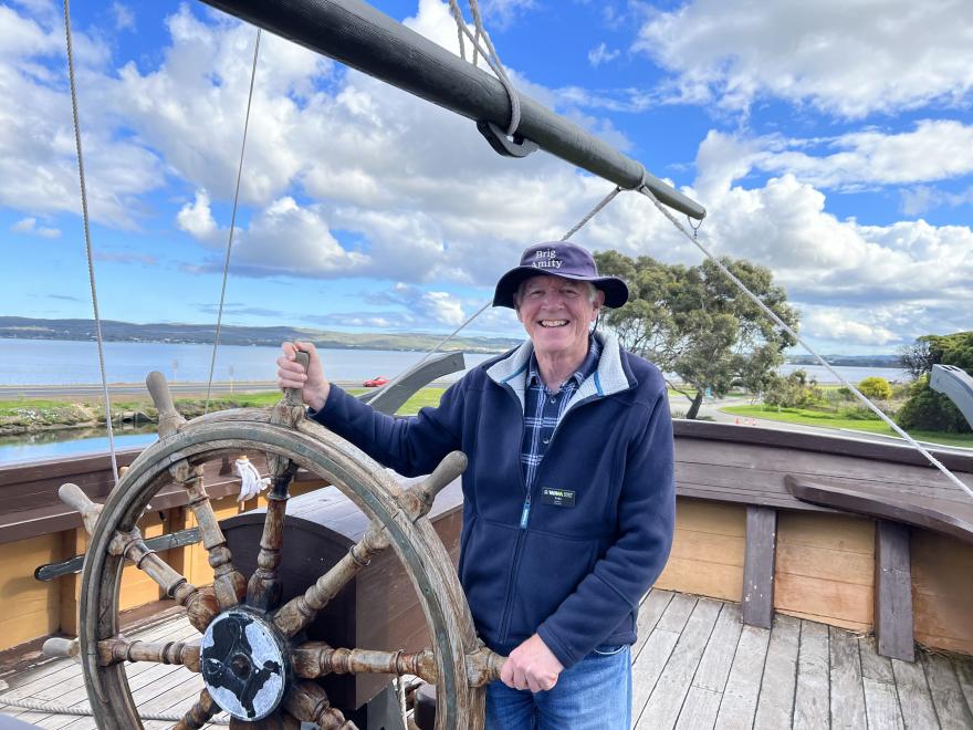 Brig Amity Volunteer Colin Berry behind the ships wheel