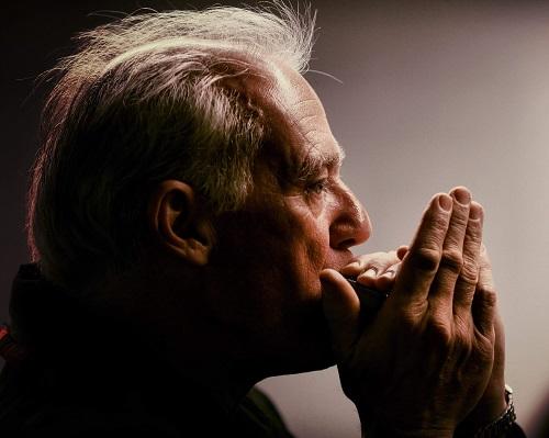 a side portrait of an adult person with short hair playing a harmonica