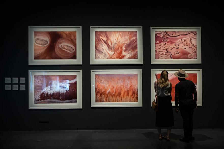 Two people stand looking at six large scale aerial photographs in a gallery