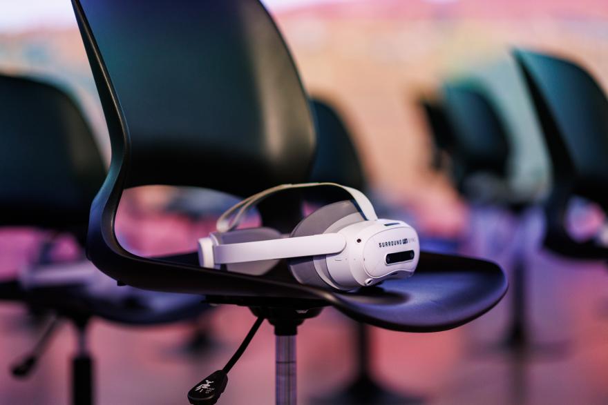 White VR headset on a black chair with blurred chairs in the background.