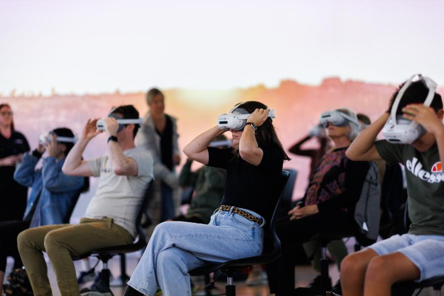People seated wearing virtual reality headsets in a room with a warm, gradient background.