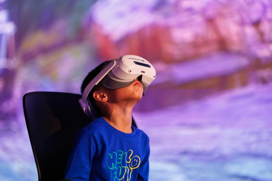 Child wearing a virtual reality headset and a blue shirt with "HELLO FUN" text.