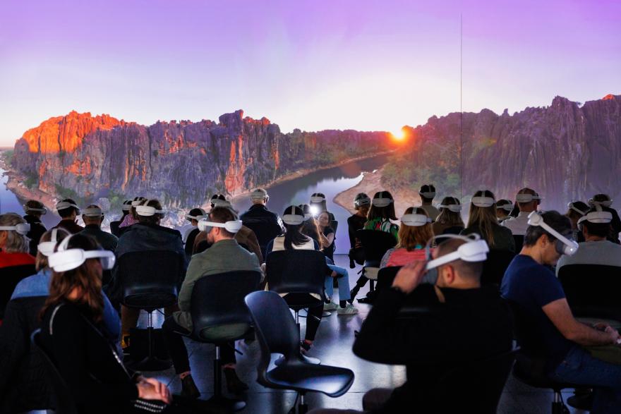 People wearing VR headsets watching a panoramic landscape of cliffs and a river at sunset.
